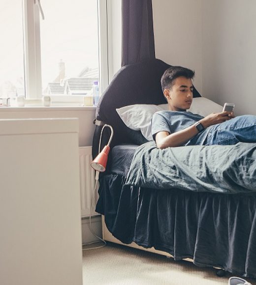 Teenage boy lying on his bed at home using a smart phone.